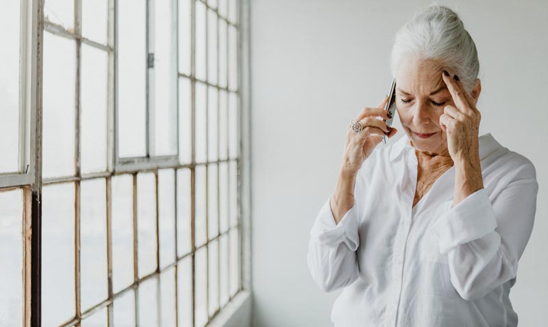 Eine ältere Frau, die mit einem Handy telefoniert und sich mit der anderen Hand an die Schläfe greift.
(c) AdobeStock