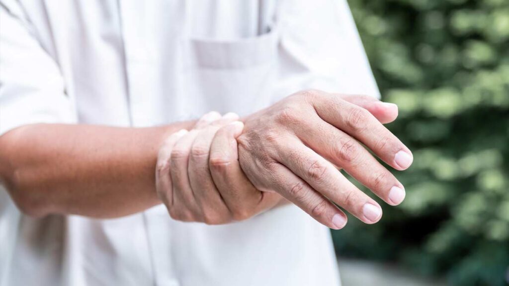 Ein Mann, der seine zitternde Hand mit der anderen hält. (c) AdobeStock