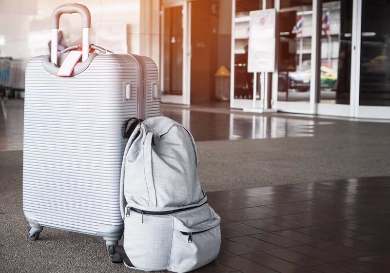 Ein Koffer und ein Rucksack vor dem Eingang zu einem Flughafen.
(c) AdobeStock