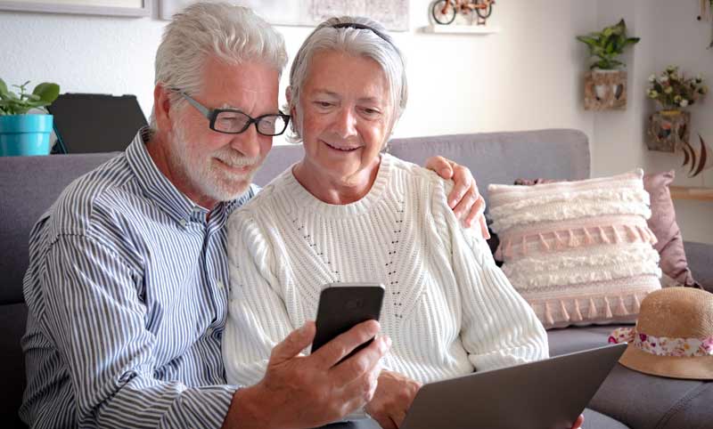 Ein älteres Paar auf der Couch, sie mit Laptop, er mit Smartphone. Beide schauen sich am Smartphone was an.
(c) AdobeStock