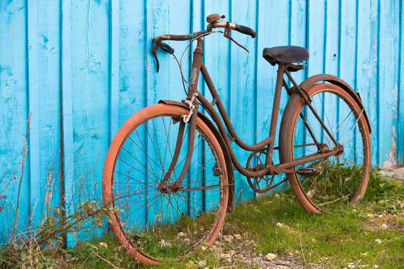 Ein altes rostiges Fahrrad lehnt an einer blau gestrichenen Holzwand.
(c) AdobeStock