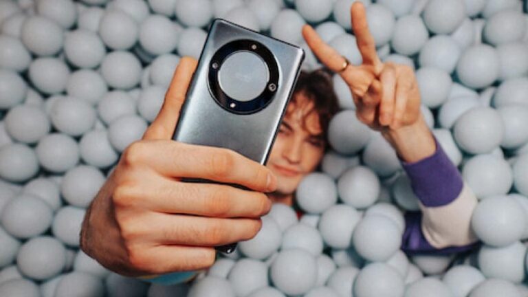 Ein Mann, der versunken in einem Bällebad mit seinem Smartphone ein Selfie macht. (c) Alterneudenken
