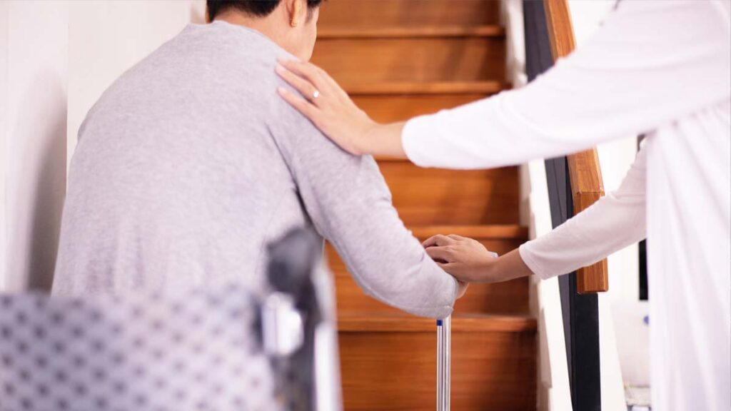 Eine Frau, die einer anderen mit Gehstock auf einer Treppe hilft. (c) AdobeStock