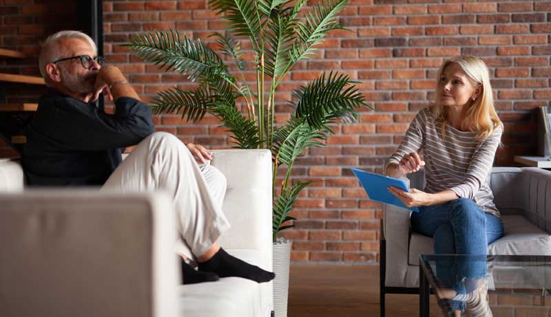 Ein Mann auf einer Couch im Gespräch mit einer Psychiaterin, die daneben in einem Sessel sitzt.
(c) AdobeStock