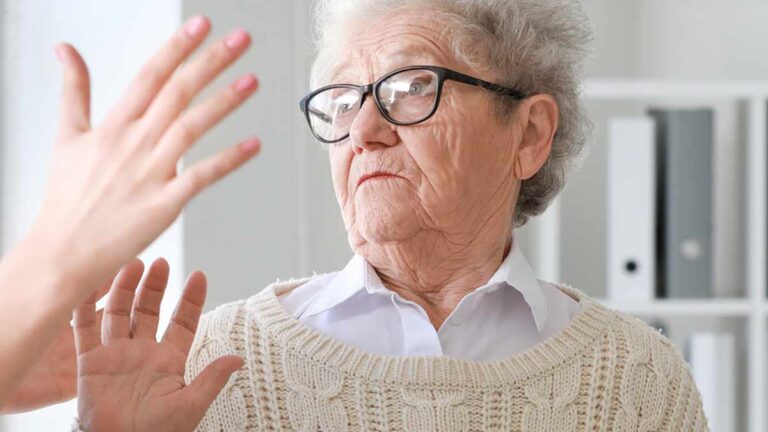 Eine ältere Frau, die den Schlag einer Pflegerin abwehrt. (c) AdobeStock