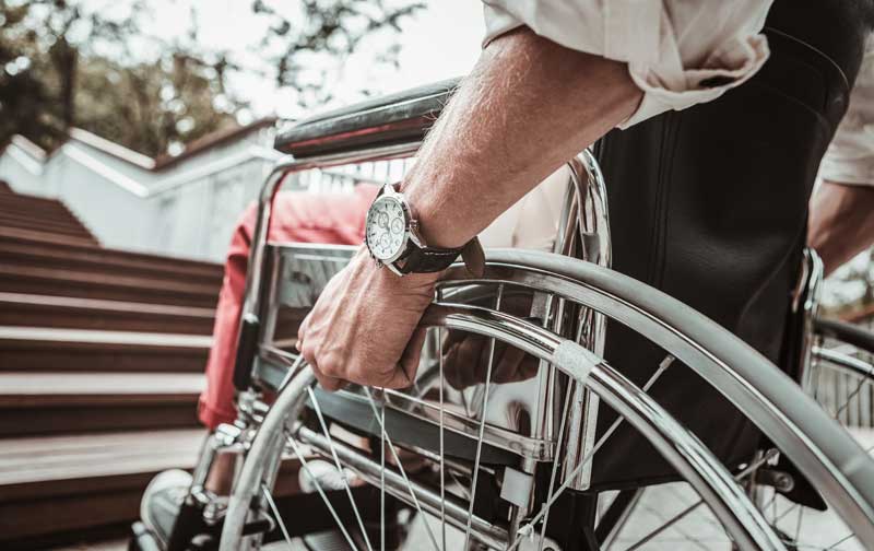 Menschen mit Behinderung erleben oft einen Urlaub mit Hindernissen 1 Die Hände eines Mannes in einem Rollstuhl vor Stufen, Stichwort Urlaub mit Hindernissen.
(c) AdobeStock