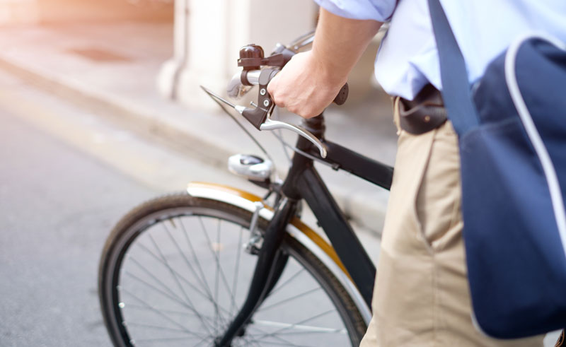 Bildausschnitt: die Hände eines Mannes, der sein Fahrrad schiebt, Stichwort aktiver Lebensstil.
(c) AdobeStock