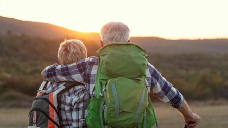 Ein älteres Paar mit Rucksack beim Betrachten eines Sonnenaufgangs in den Bergen. (c) AdobeStock