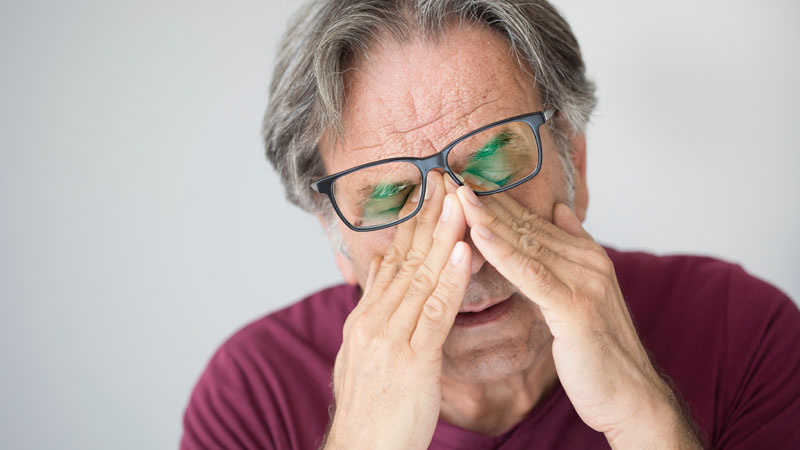 Ein Mann reibt sich vor Müdigkeit unter seiner Brille die Augen, Stichwort Eisenmangel.
(c) AdobeStock
