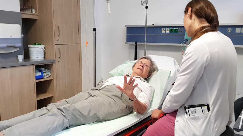 Eine ältere Frau liegt auf einem Behandlungsbett und spricht mit einer daneben sitzenden Ärztin.
(c) AdobeStock