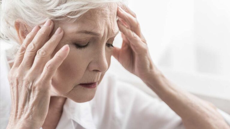 Eine ältere Frau greift sich vor Schmerzen an den Kopf. (c) AdobeStock