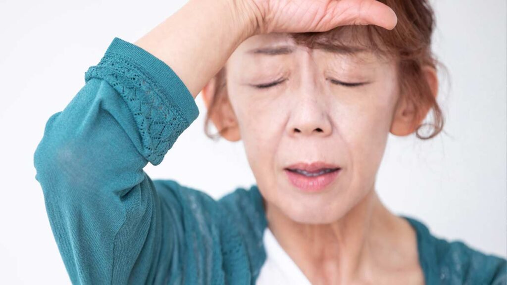 Eine Frau, die sich vor Schmerzen mit der Hand an die Stirn fasst. (c) AdobeStock