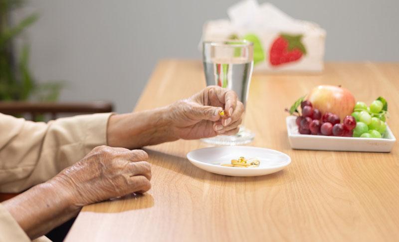 Die Hände einer alten Frau, die an einem Tisch sitzt und eine Tablette aus einem Teller nimmt, Stichwort Demenzpatient.
(c) AdobeStock