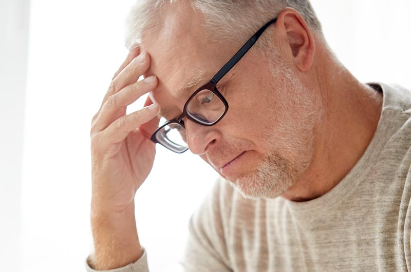 Ein Mann, der sich wegen Kopfschmerzen mit einer Hand an die Stirn greift, Stichwort Migräne.
(c) AdobeStock