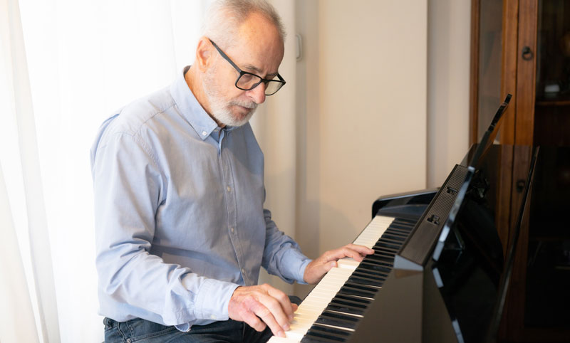 Ein älterer Mann mit Brille beim Klavierspielen, Stichwort Musikinstrument.
(c) AdobeStock