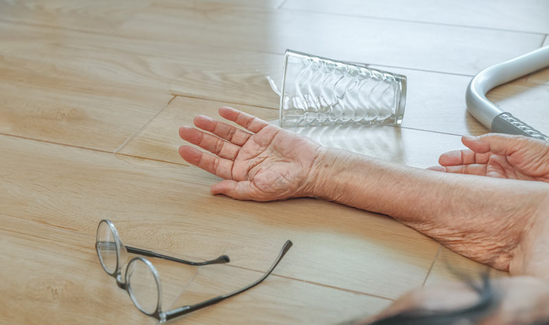 Die Hände einer gestürzten alten Frau am Boden, daneben ein umgestürztes Glas Wasser und eine Brille.
(c) AdobeStock