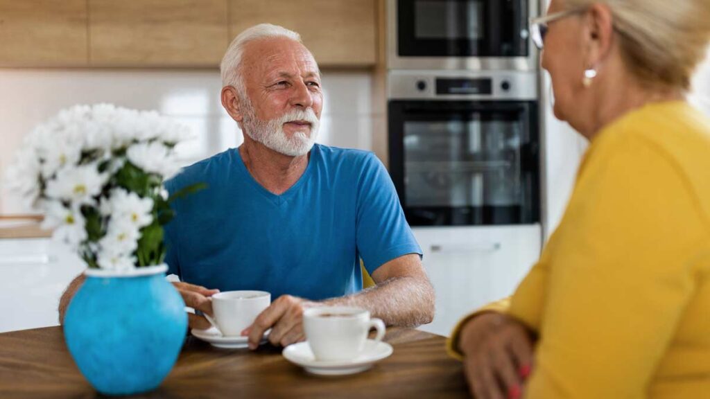 Ein älteres Paar zu Hause am Küchentisch bei einer Tasse Kaffee. (c) AdobeStock