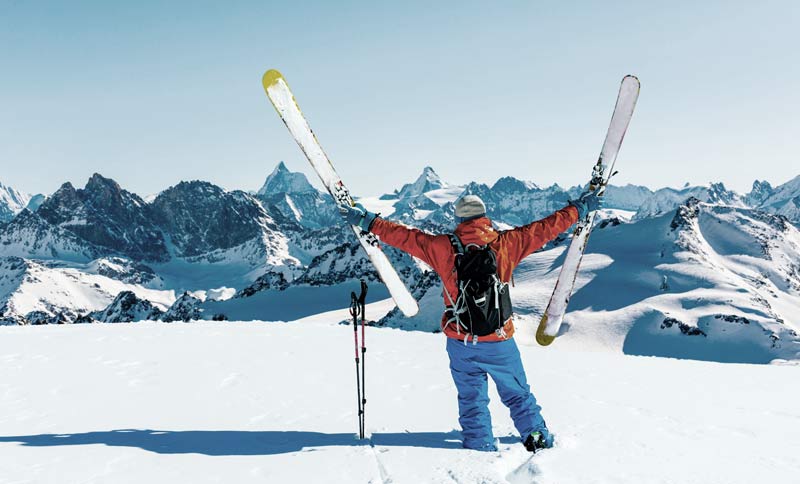 Ein Tourengeher, der seine Schi vor einer verschneiten Bergkulisse in die Höhe streckt, Stichwort Skitouren.
(c) AdobeStock