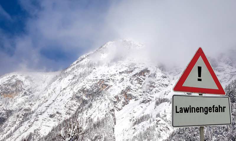 Verschneite Berge, im Vordergrund ein Warnschild "Lawinengefahr".
(c) AdobeStock