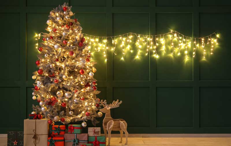 Weihnachtsbaum mit Geschenken, Lichterkette und einem Rentier.
(c) AdobeStock