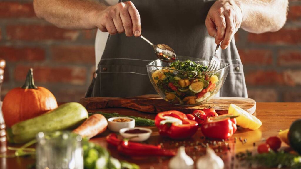 Die Hände eines Mannes in einer Küche, der sich gerade einen Salat macht. (c) AdobeStock