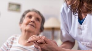 Eine Pflegerin, die die Hand einer alten Frau hält. (c) AdobeStock