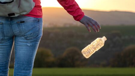 Eine Frau, die eine Plastikflasche in der Natur wegwirft. (c) AdobeStock