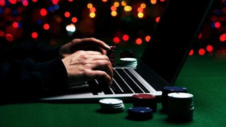 Die Hände eines Mannes auf einer Laptoptastatur, daneben Jetons. (c) AdobeStock