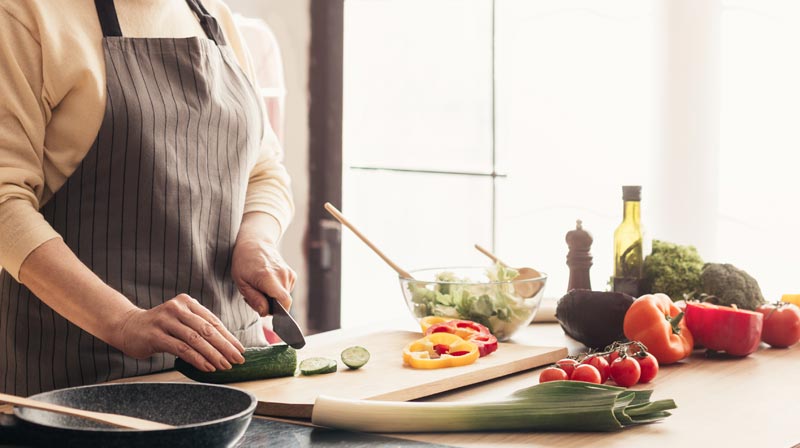 Ernährungsempfehlungen: mehr Hülsenfrüchte, weniger Fleisch, Fisch und Milchprodukte 2 Eine Frau beim Kochen, die eine Gurke schneidet.
(c) AdobeStock