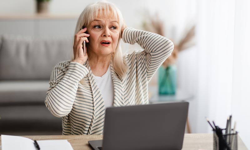 Im Netz der Betrüger – Tipps, wie man sich vor digitalen Fallen schützen kann 2 Eine ältere Frau beim Telefonieren mit einem Smartphone vor einem Laptop.
(c) AdobeStock