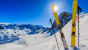 2 Ski und 2 Stecken stecken im Schnee vor atemberaubendem Winterpanorama. (c) AdobeStock