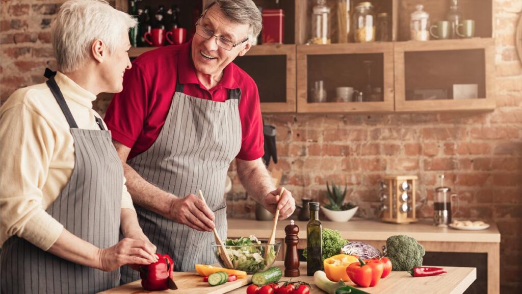 Ein älteres Paar in einer Küche beim Zubereiten eines frischen Salates. (c) AdobeStock