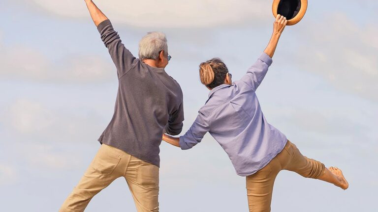 Ein älteres Paar von hinten, das vor Freude einen Luftsprung macht. (c) AdobeStock