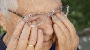 Eine ältere Frau mit Brille, die sich ihre juckenden Augen reibt. (c) AdobeStock
