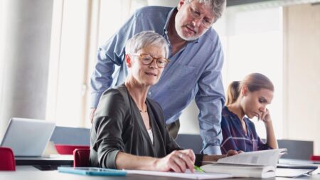 Neugier kennt kein Alter – wie lebenslanges Lernen uns bereichert und uns jung hält Eine ältere Frau mit Brille beim Machen einer Aufgabe, hinter ihr eine Lehrperson, die ihr über die Schulter schaut. (c) AdobeStock
