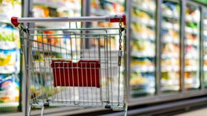 Ein leerer Einkaufswagen vor einem Kühlregal in einem Supermarkt. (c) AdobeStock
