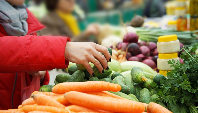 Die Hand einer Frau, die auf einem Bauernmarkt kleine Zucchini nimmt, Stichwort günstig essen.
(c) AdobeStock