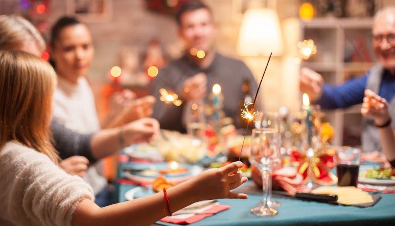 Eine Familie am Tisch zu Weihnachten beim abbrennen von Wunderkerzen.
(c) AdobeStock