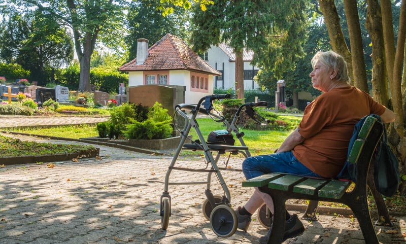 Kommunale Pflegestrategie 2026: Warum die Pflege der Zukunft Nähe braucht 2 Eine ältere Frau sitzt mit ihrem Rollator auf einer Friedhofsbank – Symbol für die Notwendigkeit barrierefreier Infrastruktur im öffentlichen Raum, Stichwort Kommunale Pflegestrategie.(c) AdobeStock