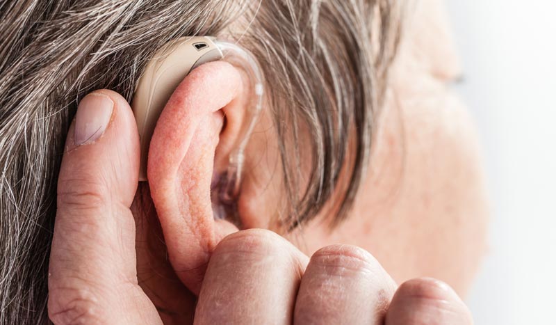 Nahaufnahme eines modernen Hinter-dem-Ohr-Hörsystems bei einem älteren Menschen mit grau meliertem Haar.(c) AdobeStock