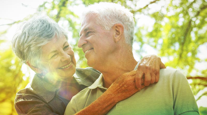 Altern »NEU« denken: Die "Bucket List der Talente" für den Neustart mit 60+ 2 Ein älteres Paar schmiegt sich im Freien lachend aneinander; das Bild ist von warmem Sonnenlicht durchflutet und zeigt einen weichgezeichneten grünen Hintergrund.(c) AdobeStock