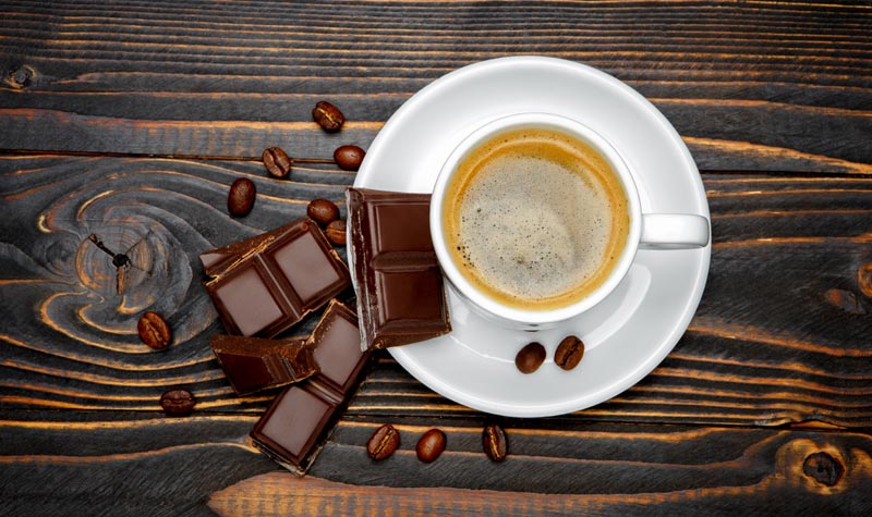 Brain-Food & Kaffee: Die 5 besten Kombinationen gegen Entzündungen 2 Eine Tasse Espresso von oben fotografiert, daneben dunkle Schokoladenstücke und Kaffeebohnen auf einem dunklen Holzhintergrund, Stichwort Brain-Food.(c) AdobeStock
