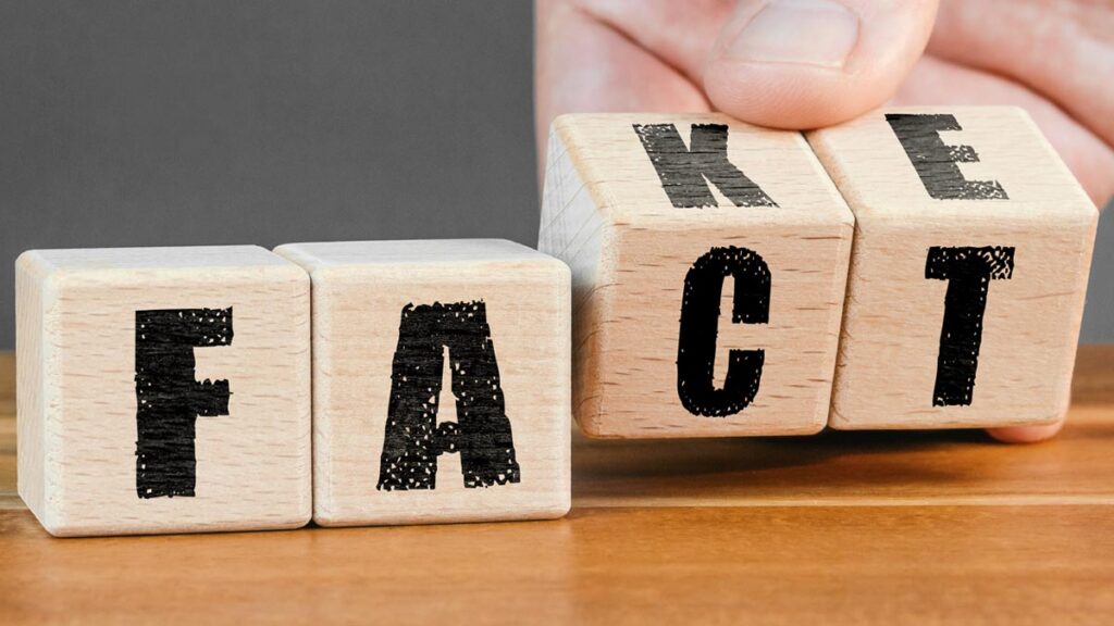 Eine Hand dreht Holzwürfel auf einem Tisch um, sodass sich das Wort „FACT“ (Fakt) in das Wort „FAKE“ verwandelt. (c) AdobeStock