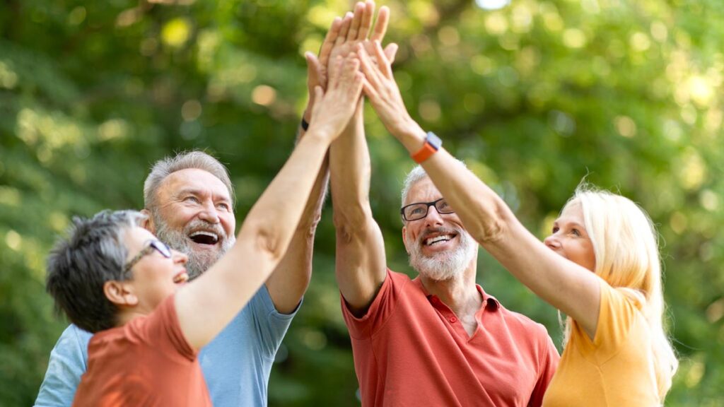 Gesundes Altern: Wie wir durch Lebenssinn und Teilhabe Vitalität gewinnen Eine Gruppe lebensfroher älterer Erwachsener im Freien, die gemeinsam die Hände zu einem High-Five heben und lachen. (c) AdobeStock