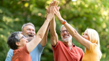 Gesundes Altern: Wie wir durch Lebenssinn und Teilhabe Vitalität gewinnen Eine Gruppe lebensfroher älterer Erwachsener im Freien, die gemeinsam die Hände zu einem High-Five heben und lachen. (c) AdobeStock