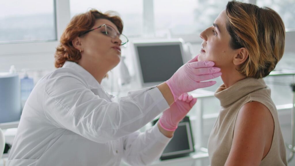 Neurodermitis und die Psyche: Warum die ganzheitliche Behandlung bei chronischem Juckreiz entscheidend ist Eine Dermatologin in weißem Kittel und rosa Handschuhen untersucht vorsichtig das Gesicht und den Hals einer Patientin in einer hellen Praxis. (c) AdobeStock