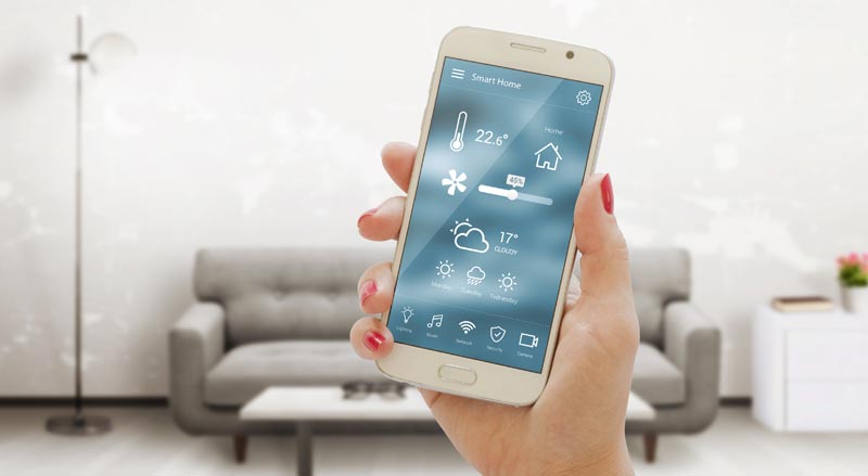 Smart Home für Senioren: 4 unschlagbare Vorteile für Ihre neue Freiheit 1 Nahaufnahme einer Hand, die ein Smartphone mit einer Smart-Home-Steuerungs-App vor einem unscharfen Wohnzimmerhintergrund hält.(c) AdobeStock