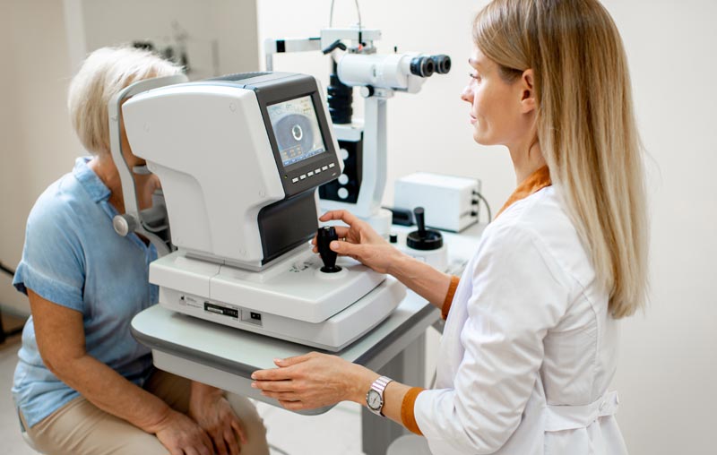 Eine Augenärztin untersucht eine ältere Patientin mit einem modernen Diagnosegerät in einer hellen Praxis.(c) AdobeStock