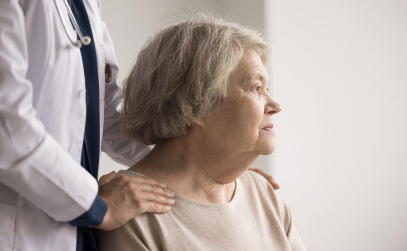 Alzheimer Prävention 2026: Die radikale Wahrheit über neue Therapien und Ihre 45%-Chance 1 Seitenansicht einer älteren Frau mit grauem Haar, die nachdenklich zur Seite blickt. Eine Person im weißen Arztkittel steht hinter ihr und legt ihr beruhigend eine Hand auf die Schulter, Stichwort Alzheimer Prävention.(c) AdobeStock