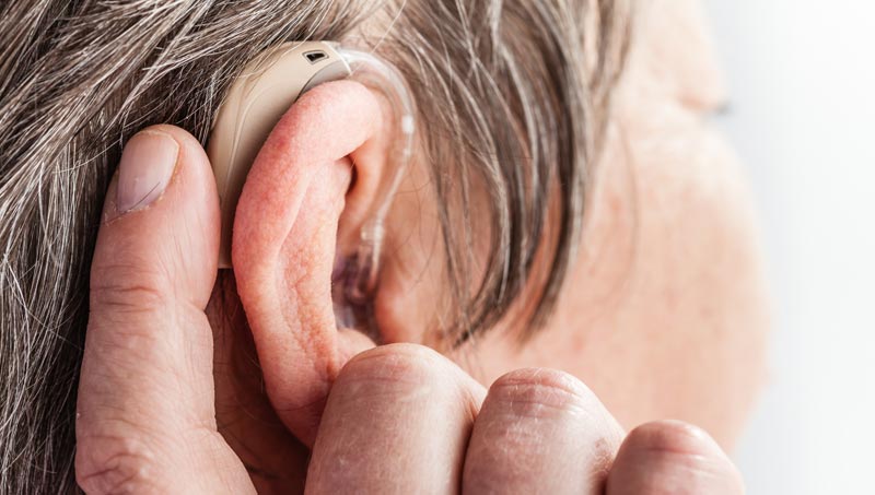 Nahaufnahme eines modernen, diskreten Hinter-dem-Ohr-Hörsystems bei einer älteren Person mit grauem Haar.
(c) AdobeStock